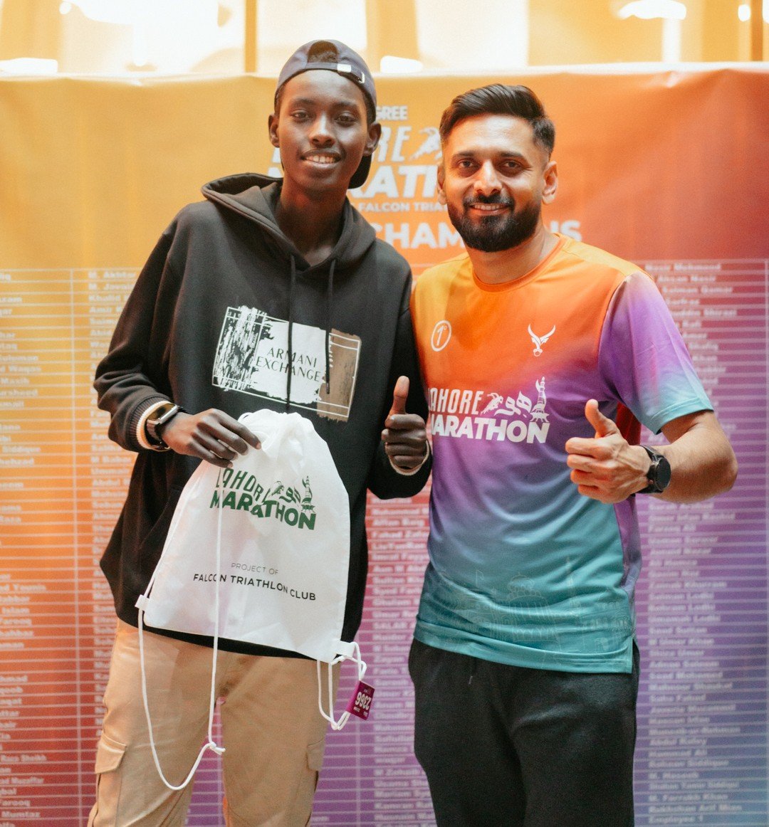 A race winner and a club member with a race bag in front of the champions wall