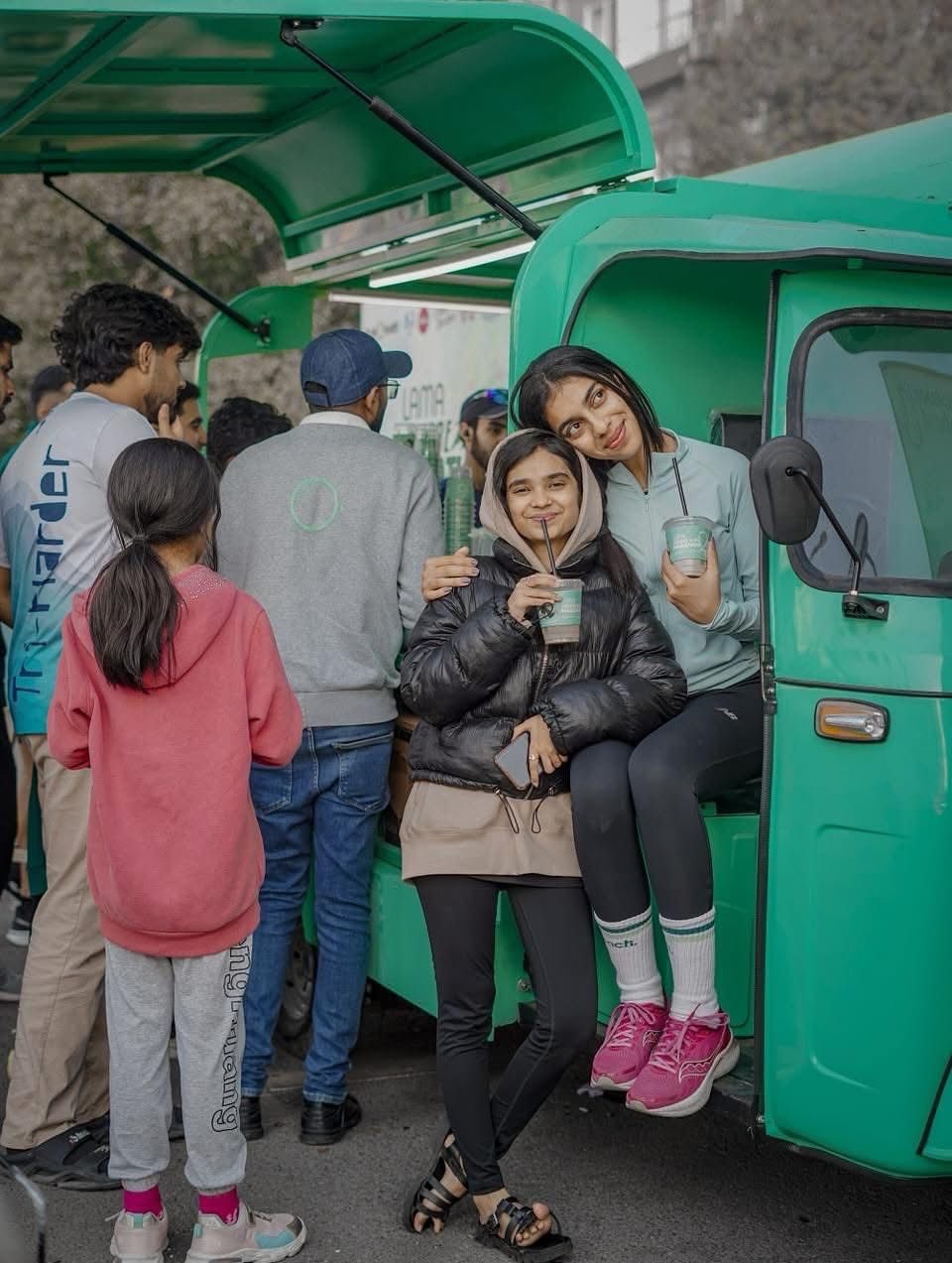 Two girls with drinks at a green stall in the Marathon Village